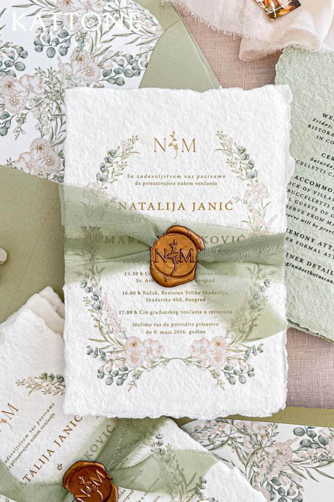Close up of handmade cotton paper invitation highlighting textured deckled edges, soft botanical wreath and elegant monogram detail.