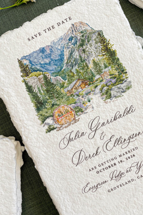 Close-up of handmade paper save the date card featuring a watercolor mountain wedding venue illustration.