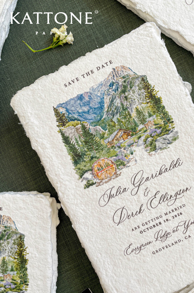 Close-up of handmade paper save the date card featuring a watercolor mountain wedding venue illustration.