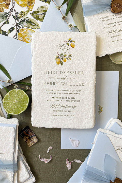 Flat lay of luxury wedding stationery including handmade paper invitations, RSVP cards, envelopes, and lemon-themed watercolor details.