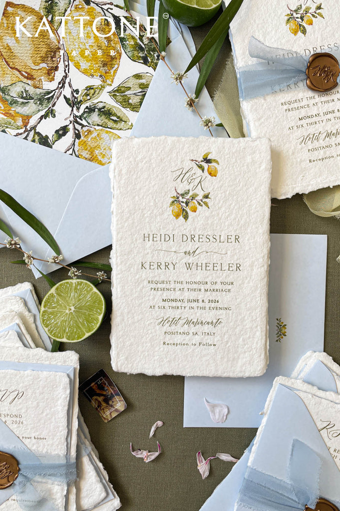 Flat lay of luxury wedding stationery including handmade paper invitations, RSVP cards, envelopes, and lemon-themed watercolor details.
