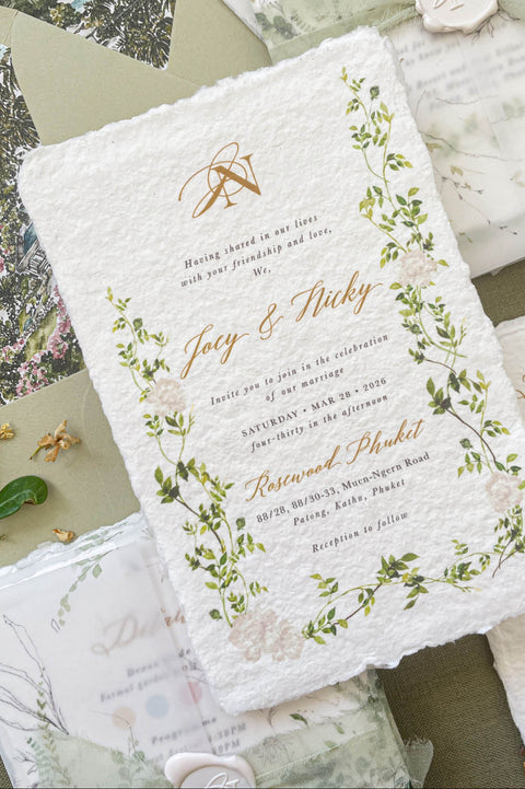 Close-up of handmade paper wedding invitation featuring botanical greenery artwork and textured deckle edges.