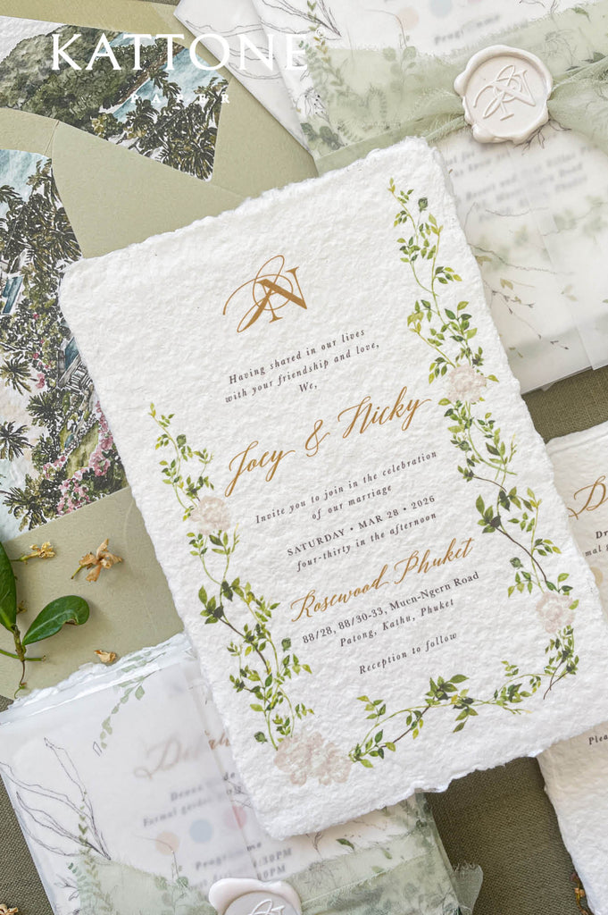 Close-up of handmade paper wedding invitation featuring botanical greenery artwork and textured deckle edges.