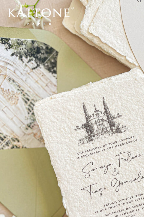 Close-up of handmade cotton paper wedding invitation featuring a watercolor illustration of a European wedding venue.