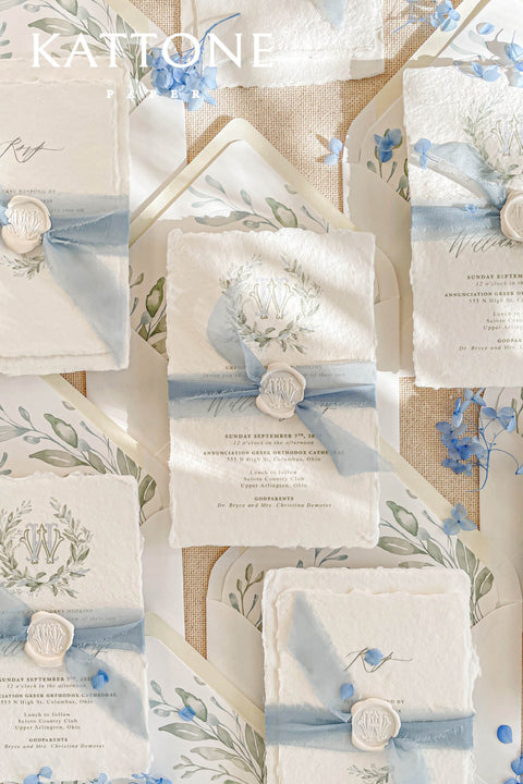 A serene baptism invitation handcrafted from luxurious handmade paper and finished with soft blue silk ribbon and a classic wax seal. Delicate watercolor botanicals and refined typography create a calm, faith-inspired design that feels timeless and elegant. Perfect for baptisms and church ceremonies, this invitation offers a meaningful keepsake to celebrate this sacred moment.