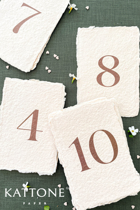 Handmade paper table numbers with deckled edges and minimalist typography, luxury wedding reception decor.