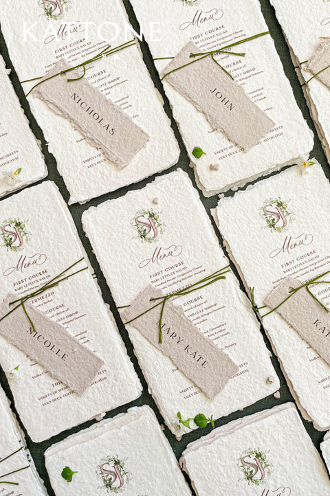 Stacked handmade paper wedding menus with watercolor monogram and deckled edges for elegant table settings.
