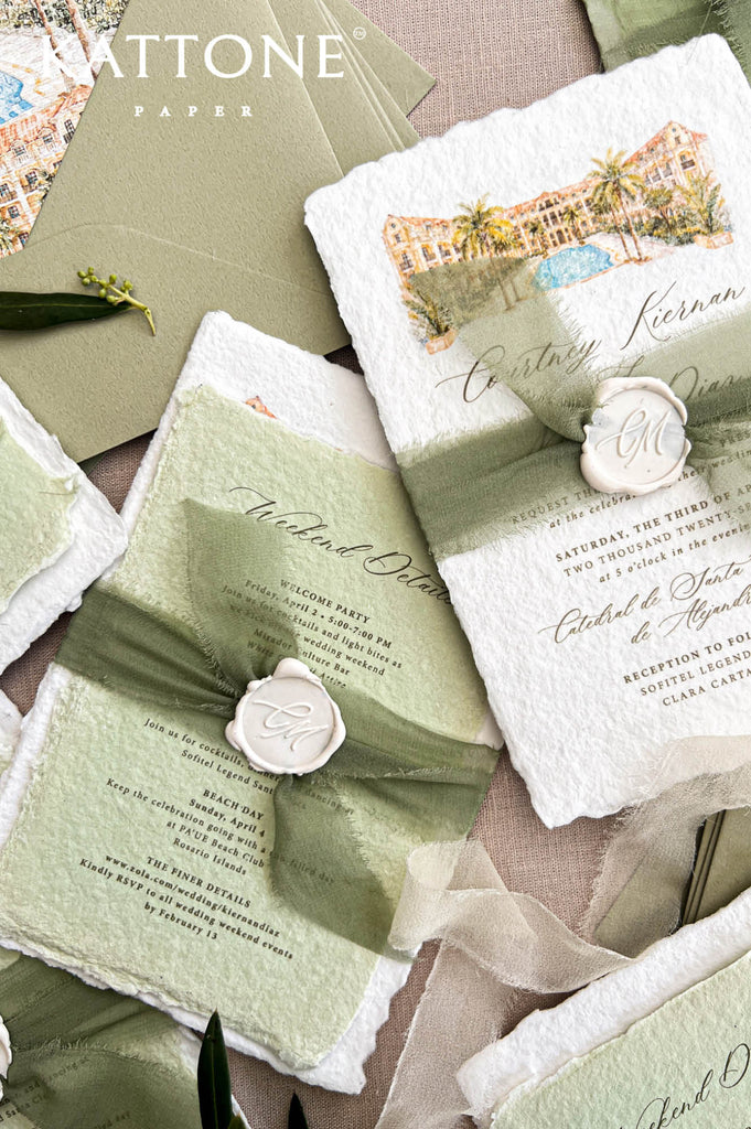Detailed overhead photograph of a pale sage green handmade paper wedding weekend details card with elegant calligraphy, ceremony and reception information, natural deckled edges, paired with an ivory watercolor wedding invitation and olive silk ribbon.