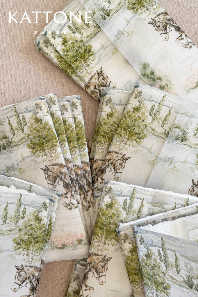 Wedding invitation wrapped in translucent vellum overlay revealing custom watercolor artwork on embossed handmade paper.