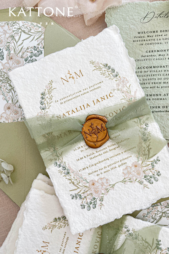 Close up of handmade cotton paper invitation highlighting textured deckled edges, soft botanical wreath and elegant monogram detail.