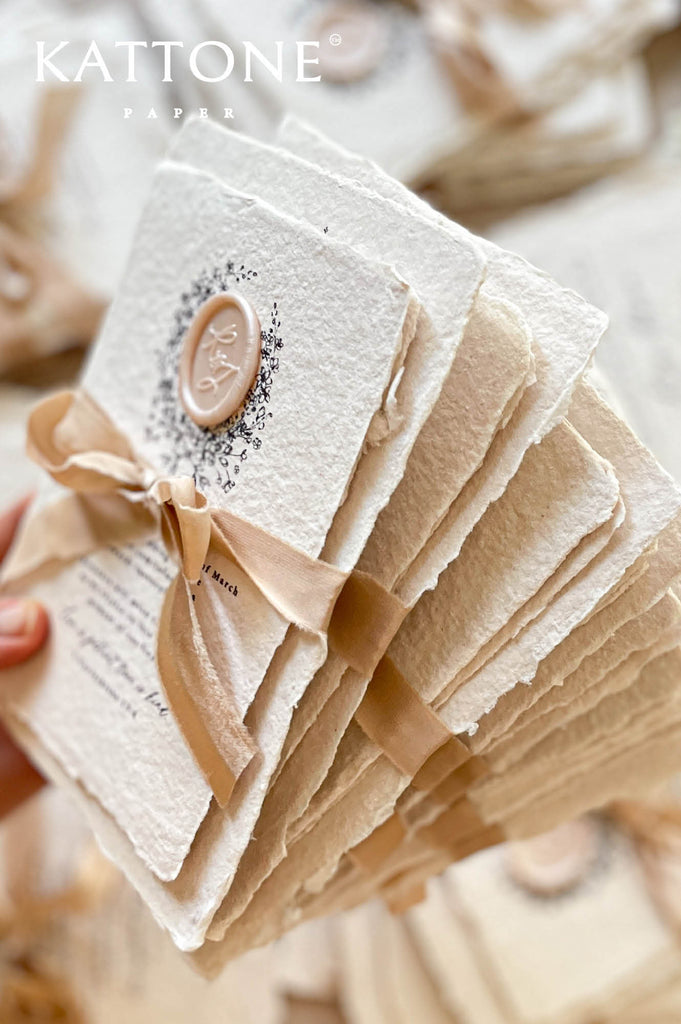 Stacked handmade paper wedding invitations and enclosure cards showcasing deckle edges and heirloom stationery quality.