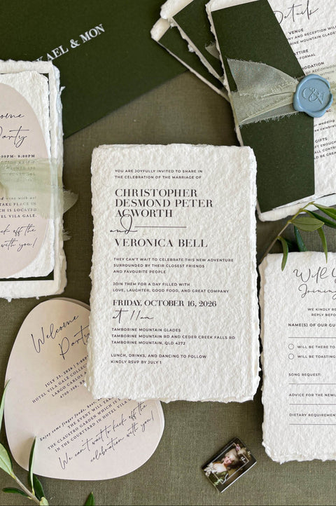 Handmade paper wedding invitation suite with deckle edges, forest green envelopes, wax seal, and modern elegant typography.
