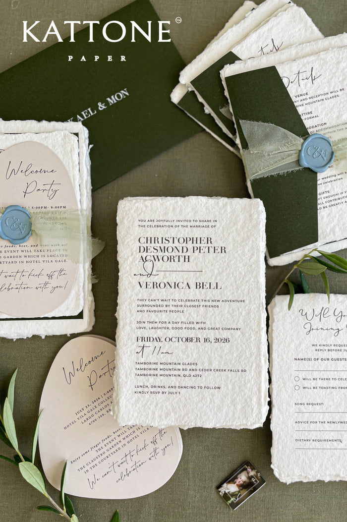 Handmade paper wedding invitation suite with deckle edges, forest green envelopes, wax seal, and modern elegant typography.
