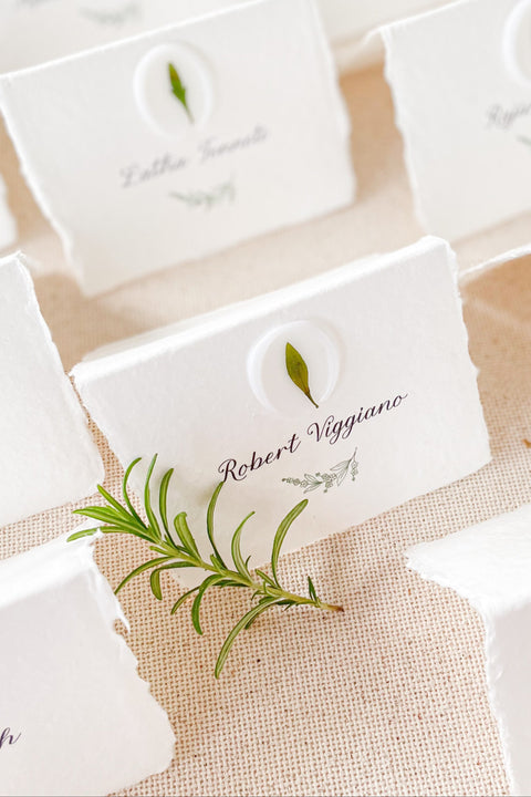 Add an organic, fine-art touch to your event with our handmade paper place cards, crafted from luxurious cotton rag paper with naturally torn deckled edges. Each card features a white botanical wax seal embedded with a real leaf, paired with elegant calligraphy for a soft, romantic aesthetic. Perfect for weddings, garden celebrations, and refined gatherings, these artisan-crafted place cards bring natural beauty and timeless charm to any tablescape.