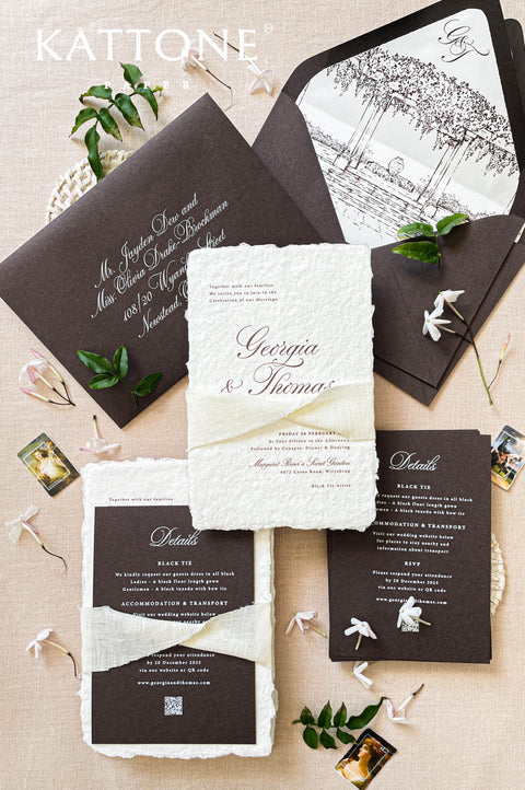 Handmade paper wedding invitation with deckled edges, charcoal envelope, silk ribbon wrap, elegant black tie wedding stationery flat lay.