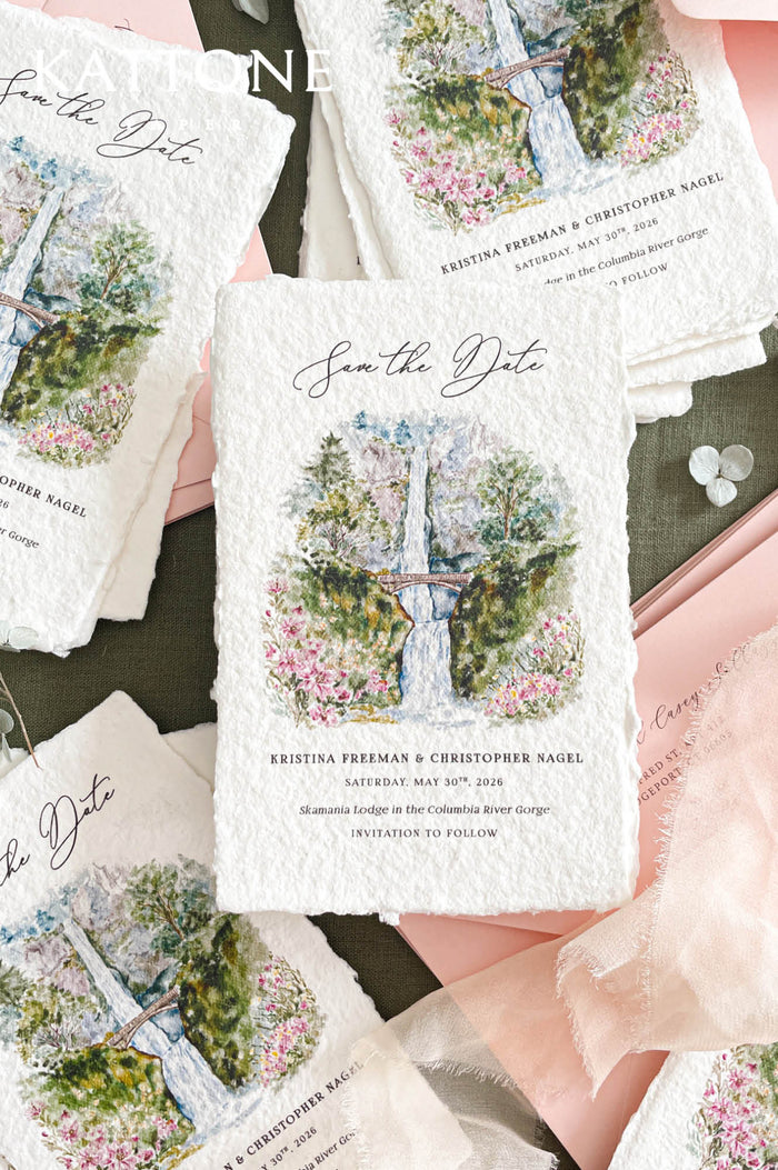 Handmade save the date card with deckled edge cotton paper featuring watercolor landscape illustration of waterfall, bridge and florals, elegant calligraphy typography and fine art wedding stationery style.