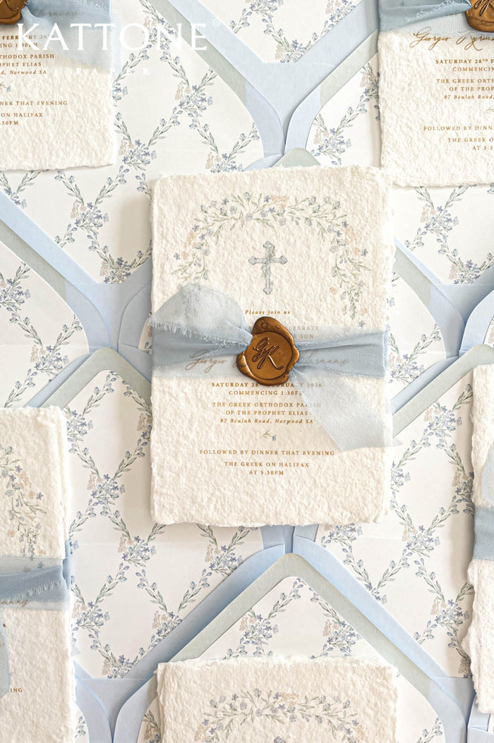 Christian handmade paper wedding invitation with botanical cross design, blue silk ribbon, and wax seal.