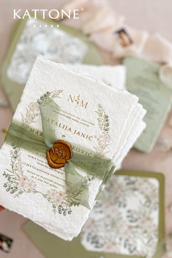Close up of handmade cotton paper invitation highlighting textured deckled edges, soft botanical wreath and elegant monogram detail.