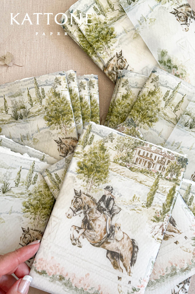 Wedding invitation wrapped in translucent vellum overlay revealing custom watercolor artwork on embossed handmade paper.