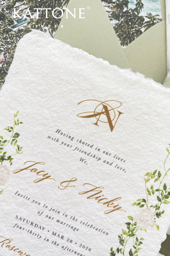 Close-up of handmade paper wedding invitation featuring botanical greenery artwork and textured deckle edges.