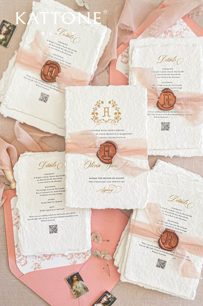 Handmade paper wedding invitations with custom monogram crest, blush silk ribbon, wax seal detail, and deckle edge cotton paper.