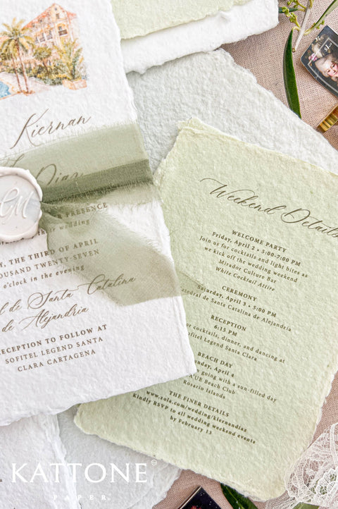 Angled close-up of a white deckled handmade paper wedding invitation featuring a custom watercolor resort illustration, elegant calligraphy, sage green silk ribbon and personalized ivory wax seal, styled beside a matching green weekend itinerary card.