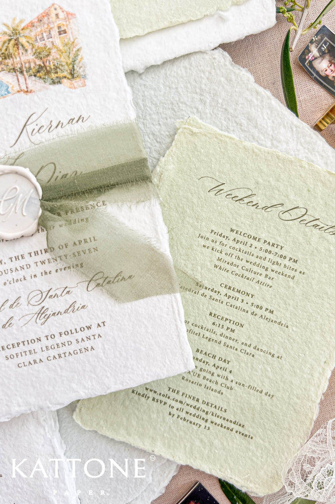 Angled close-up of a white deckled handmade paper wedding invitation featuring a custom watercolor resort illustration, elegant calligraphy, sage green silk ribbon and personalized ivory wax seal, styled beside a matching green weekend itinerary card.