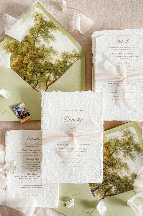 Luxury handmade paper wedding invitation suite featuring deckled edge cotton paper, ivory chiffon ribbon, sage green envelopes, custom scenic envelope liners, and elegant fine art wedding stationery styling.