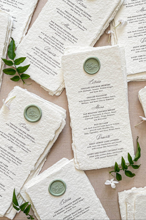 Stacked handmade paper wedding menus with deckled edges and wax seal details for elegant table settings.