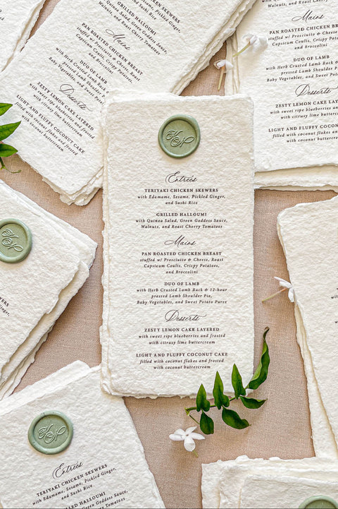 Handmade paper wedding menu with deckled edges and custom wax seal, fine art reception stationery flat lay.