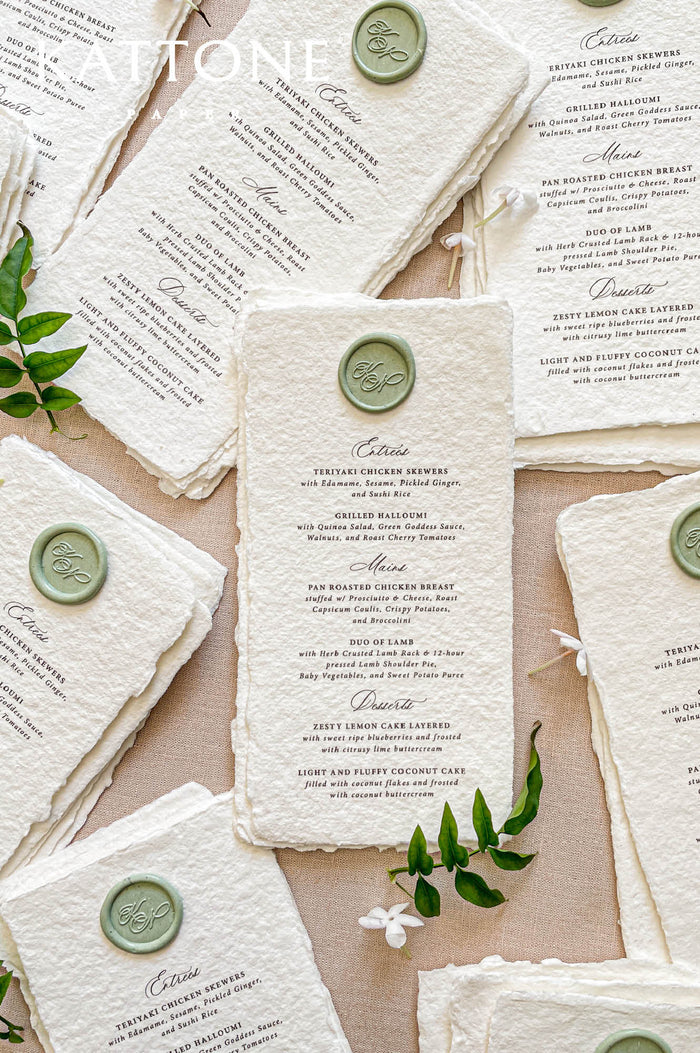 Handmade paper wedding menu with deckled edges and custom wax seal, fine art reception stationery flat lay.