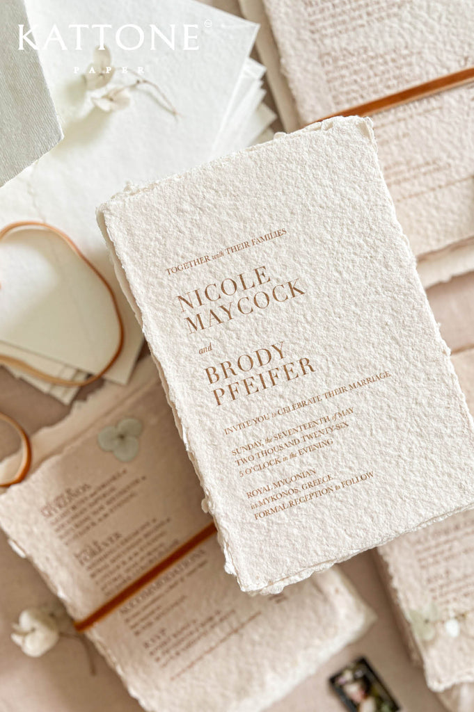 Close up of textured handmade cotton paper invitation highlighting organic deckled edges and modern serif typography in warm neutral tones.