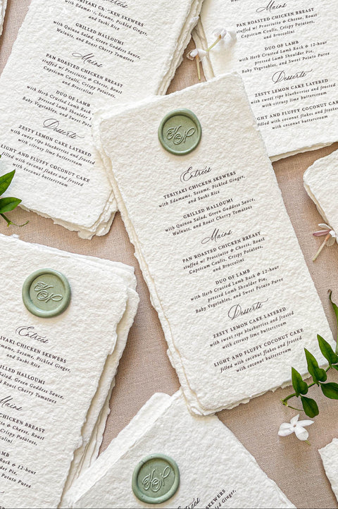 Close-up of handmade cotton paper wedding menu featuring green wax seal monogram and elegant typography.