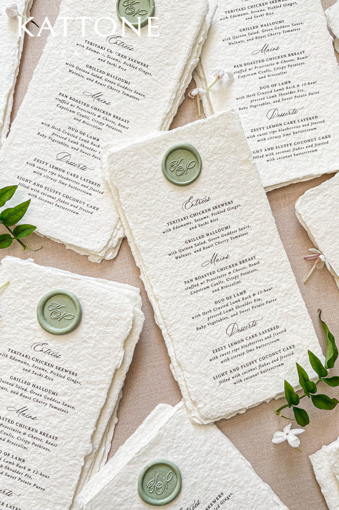 Close-up of handmade cotton paper wedding menu featuring green wax seal monogram and elegant typography.