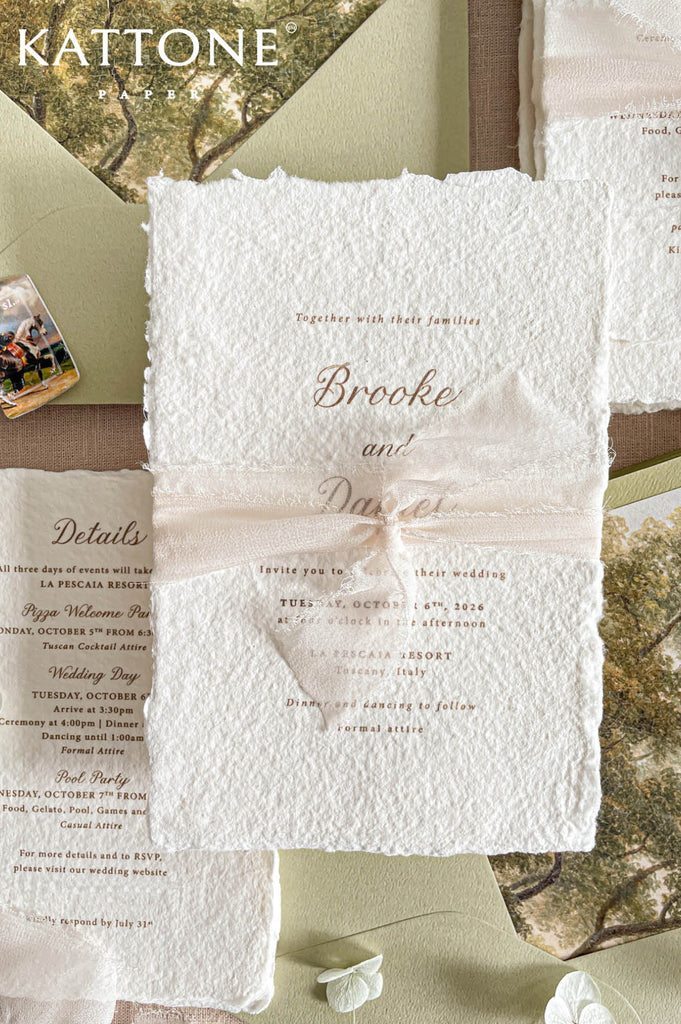 Romantic flat lay of luxury wedding stationery showcasing handmade paper invitations, scenic envelope liners, chiffon ribbon styling, details cards, and coordinating inserts.
