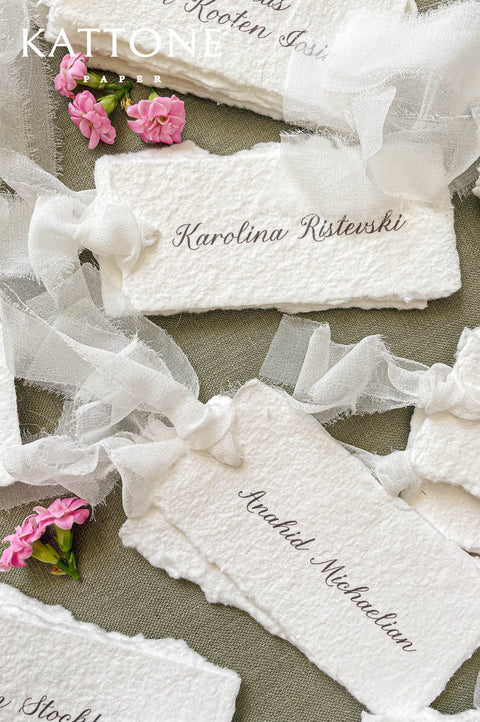 Close-up of handmade cotton paper place card tied with sheer silk ribbon, romantic wedding table stationery.