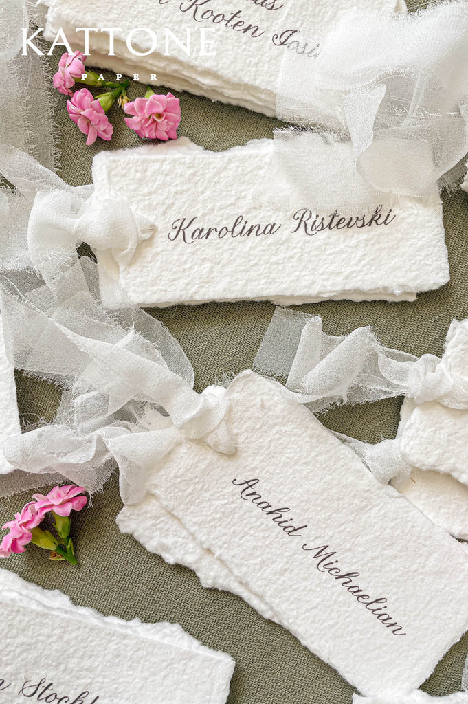 Close-up of handmade cotton paper place card tied with sheer silk ribbon, romantic wedding table stationery.