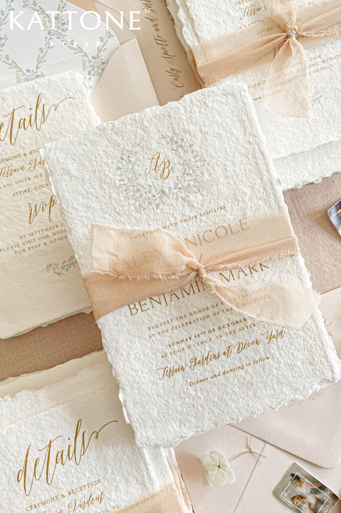Elegant handmade paper wedding invitation with deckled edges featuring refined typography, soft botanical crest artwork, and romantic blush ribbon styling for a timeless luxury wedding aesthetic.