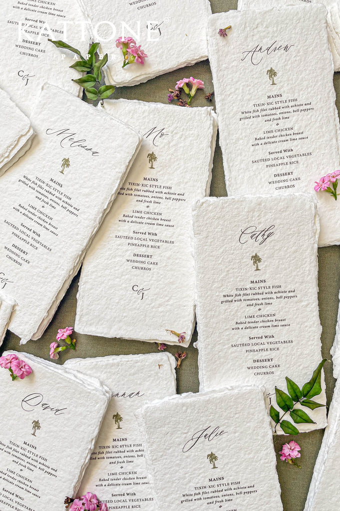 Stacked handmade paper wedding menus with guest names and icon motif for elegant table settings.