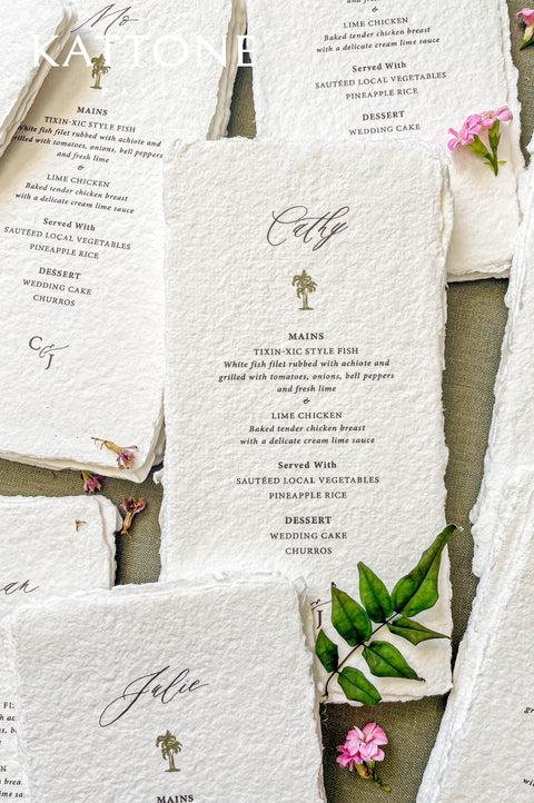 Handmade paper wedding menu with deckled edges, personalized guest name, elegant icon motif, fine art reception stationery flat lay.