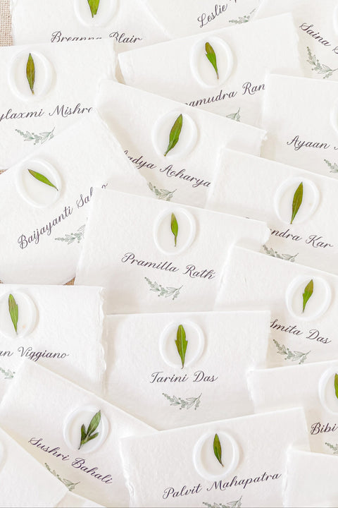 Add an organic, fine-art touch to your event with our handmade paper place cards, crafted from luxurious cotton rag paper with naturally torn deckled edges. Each card features a white botanical wax seal embedded with a real leaf, paired with elegant calligraphy for a soft, romantic aesthetic. Perfect for weddings, garden celebrations, and refined gatherings, these artisan-crafted place cards bring natural beauty and timeless charm to any tablescape.