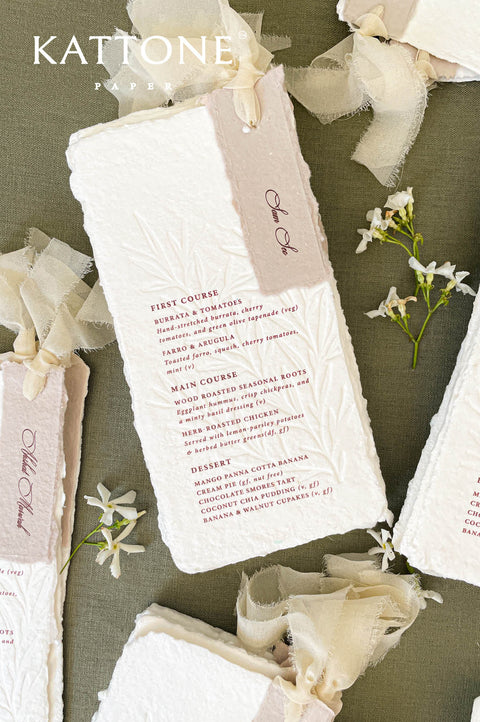 Handmade paper wedding menus tied with soft ribbon for an elegant reception table presentation.