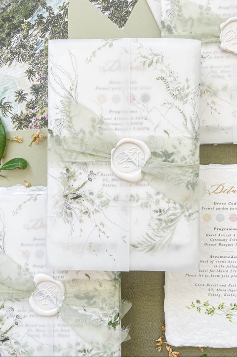 Wedding invitation wrapped in translucent vellum revealing botanical watercolor artwork on handmade paper.