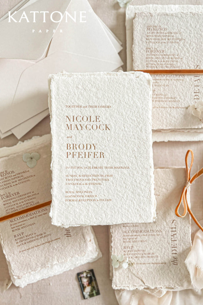 Luxury handmade cotton paper wedding invitation with deckled edges and warm terracotta typography, styled with neutral envelopes, ribbon accents and coordinated stationery suite on soft beige background.