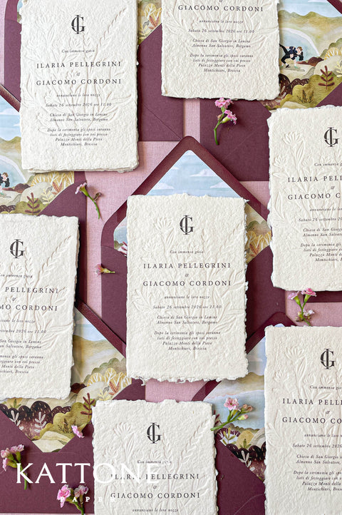 Embossed handmade paper wedding invitation with deckled edges, soft botanical relief, elegant serif typography, romantic European wedding stationery flat lay.