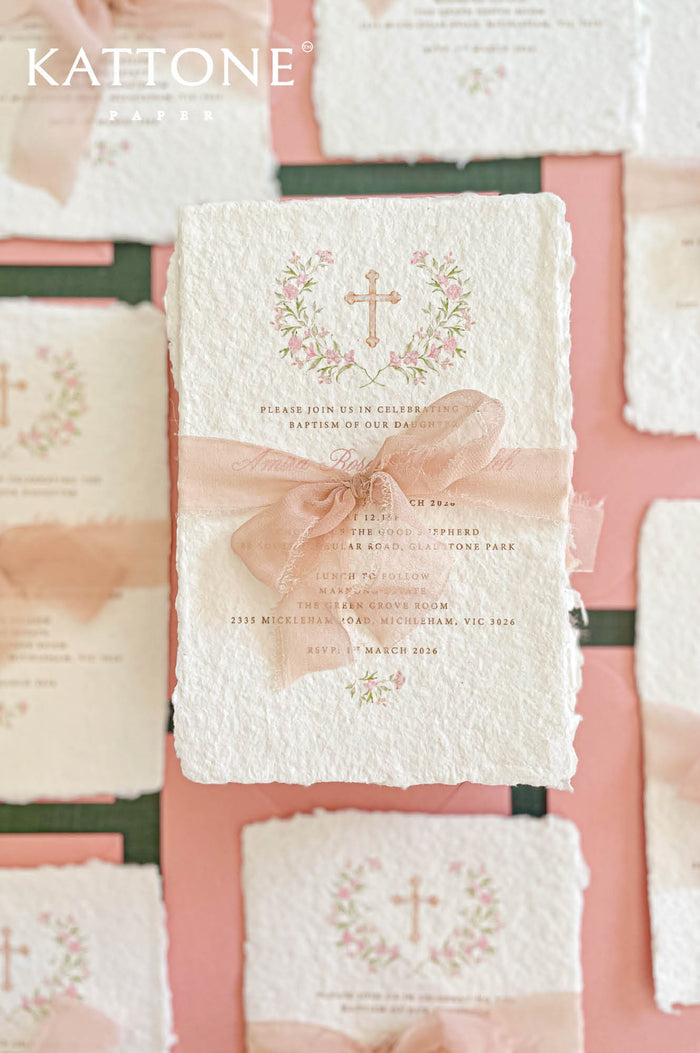 Christian baptism invitation printed on handmade cotton paper with floral cross design and blush silk ribbon.