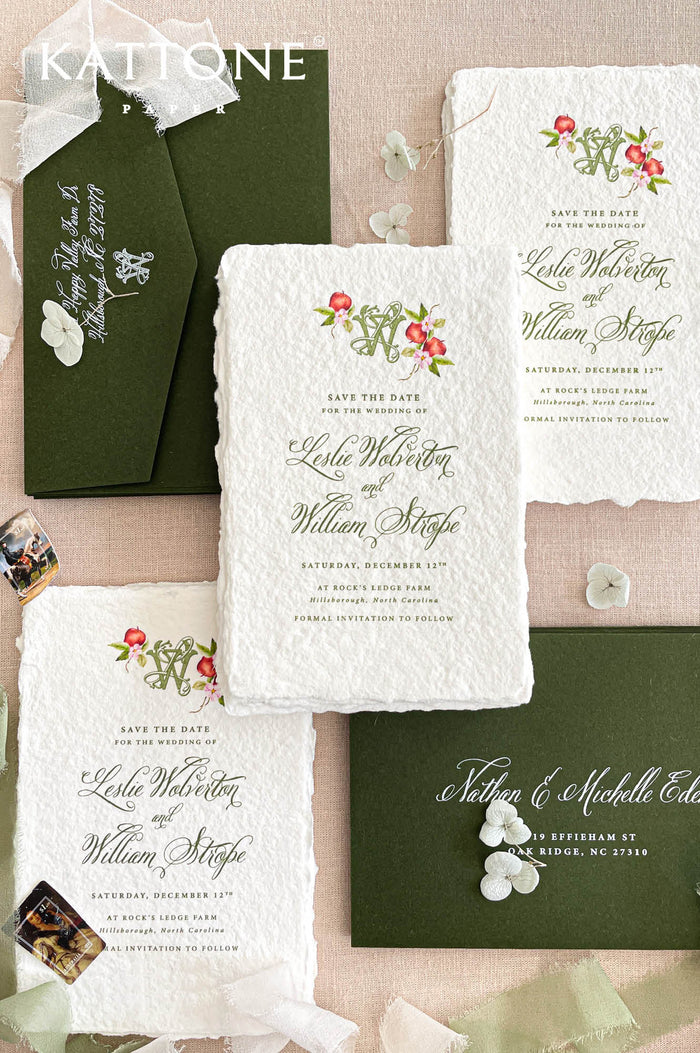 Handmade paper save the date cards with deckled edges, floral monogram and dark green envelopes styled on neutral linen background.