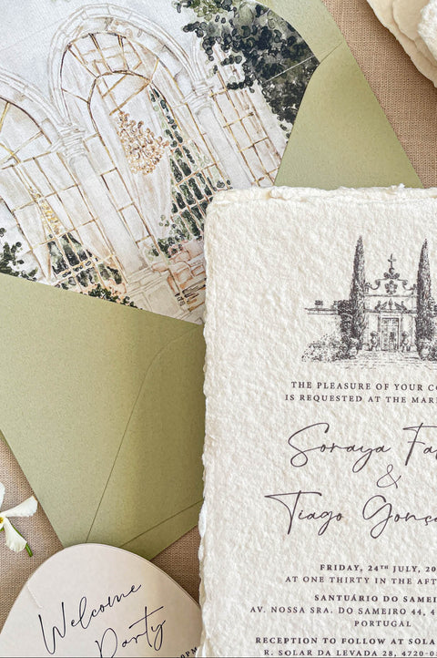 Close-up of handmade cotton paper wedding invitation featuring a watercolor illustration of a European wedding venue.