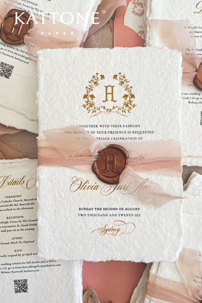 Close-up of handmade cotton paper wedding invitation featuring a gold monogram crest, textured deckle edges, and refined typography.