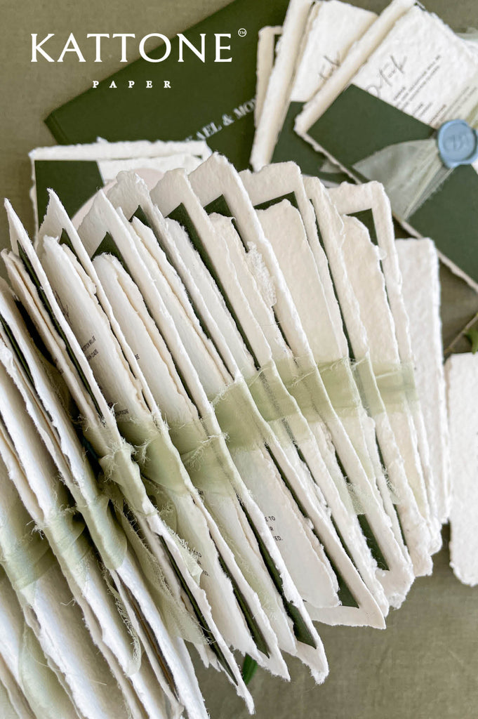 Stacked handmade paper wedding invitations and enclosure cards showcasing natural torn edges and luxury paper texture.
